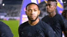 a man with a beard wearing a black shirt is standing on a soccer field with other players .