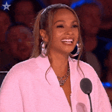 a woman wearing a pink jacket and hoop earrings is smiling in front of a microphone .