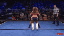 two women are wrestling in a wrestling ring with a referee in the background .