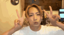 a young man in a white shirt is making a peace sign with his hands