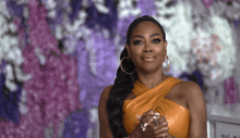 a woman in an orange dress with hoop earrings is clapping her hands
