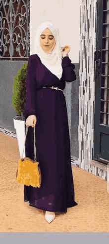a woman wearing a purple dress and a white hijab is holding a yellow purse
