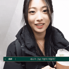 a woman in a black jacket is smiling and holding a cup with the name aran on it