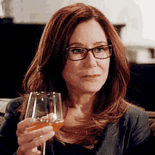 a woman with glasses is holding a wine glass