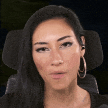 a woman wearing hoop earrings is sitting in a chair and looking at the camera