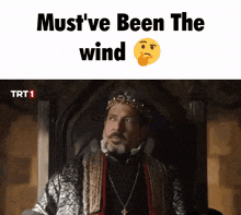 a man with a crown on his head is sitting in a chair with the words must 've been the wind written above him