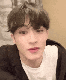 a young man wearing a white t-shirt and a black jacket is looking at the camera