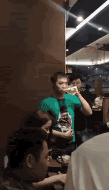 a man in a green shirt is drinking from a glass in a restaurant