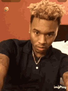 a young man with blonde hair is wearing a black shirt and a gold chain .
