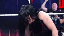 a woman in a black dress is kneeling down in a wrestling ring while a man watches .