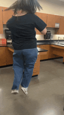 a woman in a black shirt and jeans is jumping in a kitchen