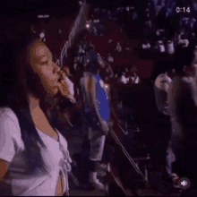 a woman is standing in front of a crowd of people at a concert and smoking a cigarette .