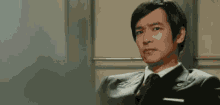 a man in a suit and tie is sitting in an elevator and making a funny face .