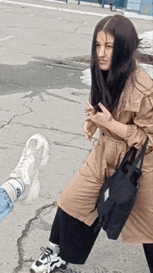 a woman in a trench coat is standing next to a person 's foot