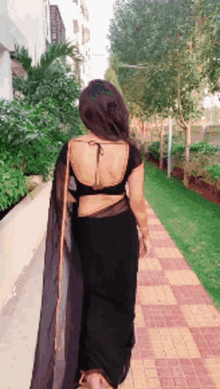 a woman in a black saree is walking down a sidewalk .