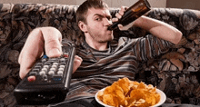 a man sitting on a couch drinking a beer and eating chips