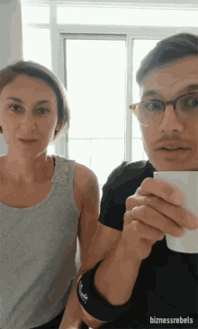 a man and a woman are standing next to each other and the man is holding a cup of coffee in his hand