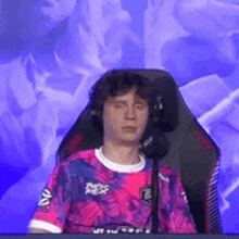 a man in a pink and blue shirt is sitting in a gaming chair .