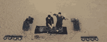 two dj 's are playing music on a sandy beach with their arms outstretched