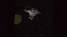 a man is sitting in a chair in a dark room while another man is standing in the background .