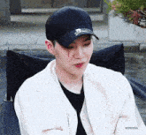 a young man wearing a black hat and a white jacket is sitting in a chair with blood running down his face .