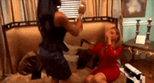 two women are having a fight in a living room while sitting on a couch .