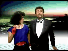 a man in a tuxedo and bow tie stands next to a woman in a blue top