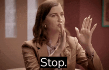a woman in a brown jacket is making a stop gesture with her hands