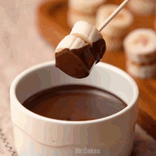 a marshmallow is dipping into a cup of chocolate sauce