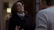a man and a woman are fighting in a living room . the woman is wearing glasses and a scarf .