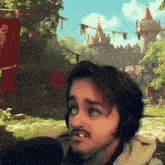 a man wearing headphones stands in front of a castle with red banners
