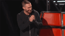 a man is laughing while singing into a microphone on a stage in front of a red chair .
