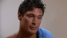 a shirtless man with a blue towel around his neck looks at the camera