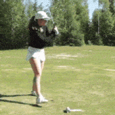 a young woman is swinging a golf club on a golf course .