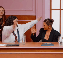 two women sitting at a table with their arms outstretched