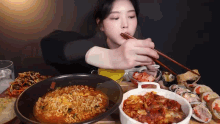 a woman is eating ramen and sushi with chopsticks at a table .