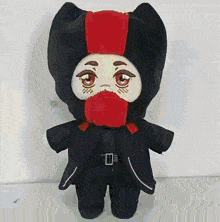 a stuffed animal with a red scarf around its neck and a black hood is standing on a white surface .