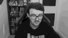 a man wearing glasses is sitting in a chair in front of a computer screen .