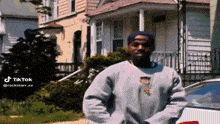 a man in a gray sweatshirt is standing in front of a white car in front of a house .