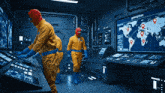 three men in yellow jumpsuits are working in a room with a large screen that says gosopticon
