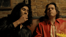 a man in a red jacket is smoking a cigarette next to another man