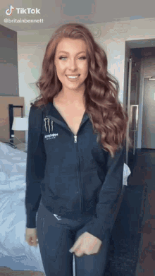 a woman wearing a monster energy hoodie is smiling in a hotel room