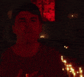a man stands in front of a row of lit candles with his eyes closed