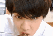 a young boy is eating something with a spoon in his mouth .