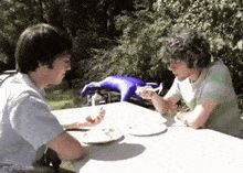 two men are sitting at a table with plates of food and talking to each other .