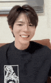 a young man wearing a black shirt with a white graphic on the front smiles
