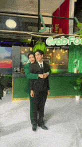 two men hugging in front of a grab food sign