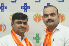 two men pose for a picture in front of a wall that says one