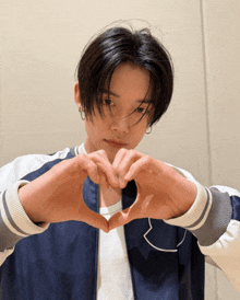a young man in a blue jacket makes a heart with his hands