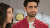 a man with a beard wearing a red jacket looks at a woman